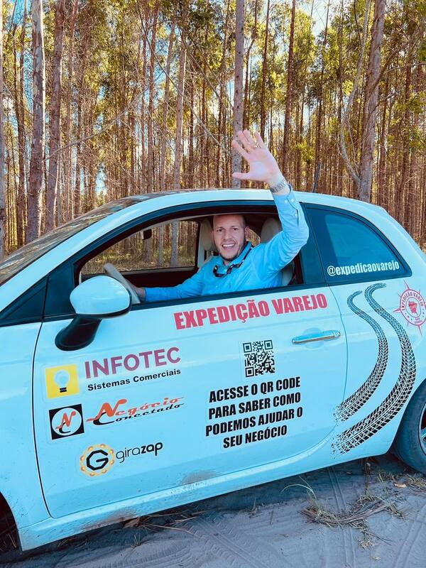 Jorge Regis acenando da janela do Fiat 500 adesivado da Expedição Varejo, numa estrada de terra